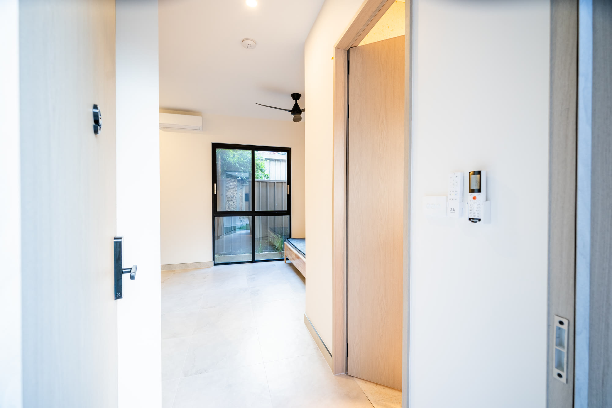 Looking into a room in a completed Auzzy Projects co-living home in Western Sydney, showing the room's own light switch and air conditioning control on the wall, its own split system, a ceiling fan and a door through to the ensuite